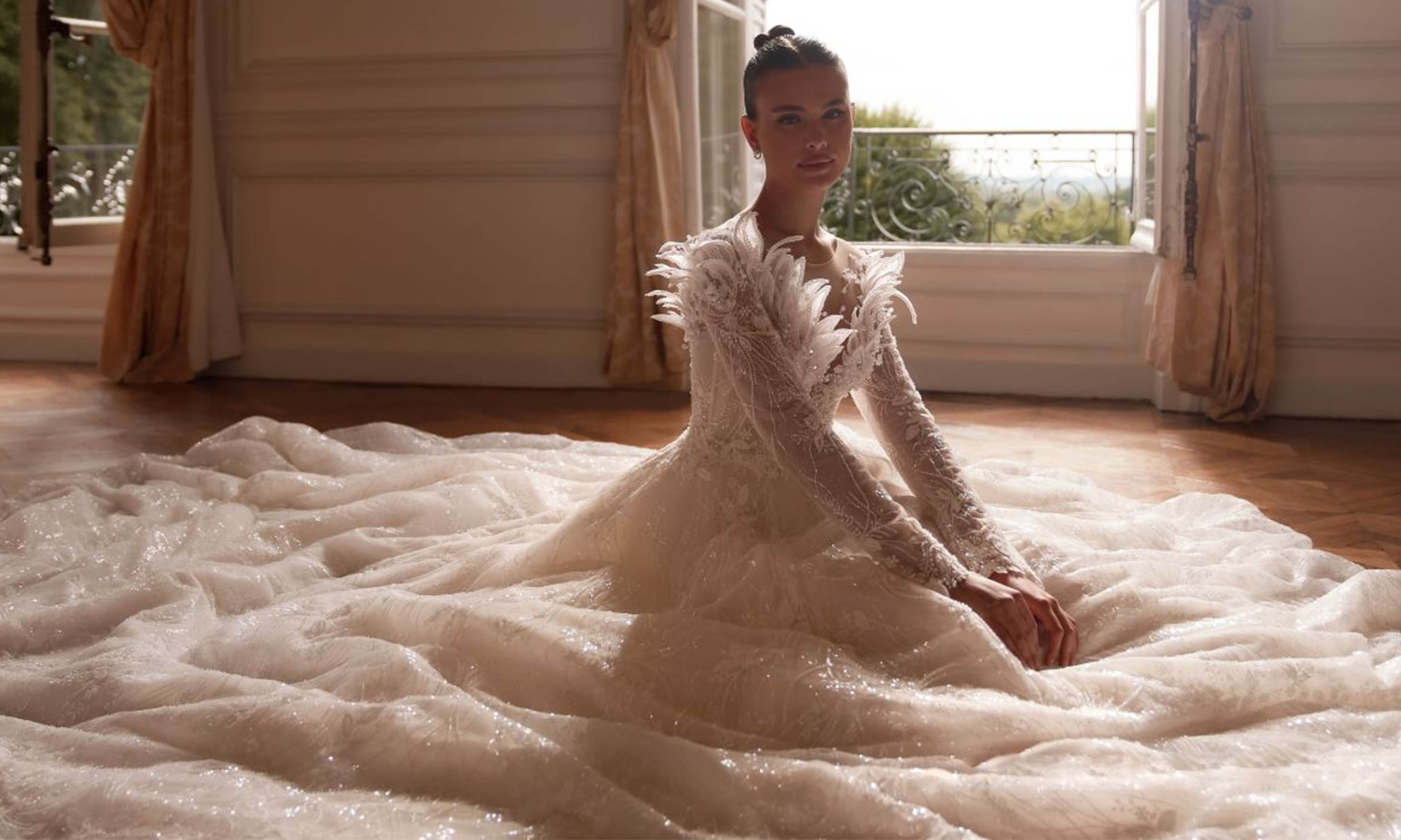 Robe de mariée princesse à manches longues ornées de plumes, jupe volumineuse et traîne circulaire.