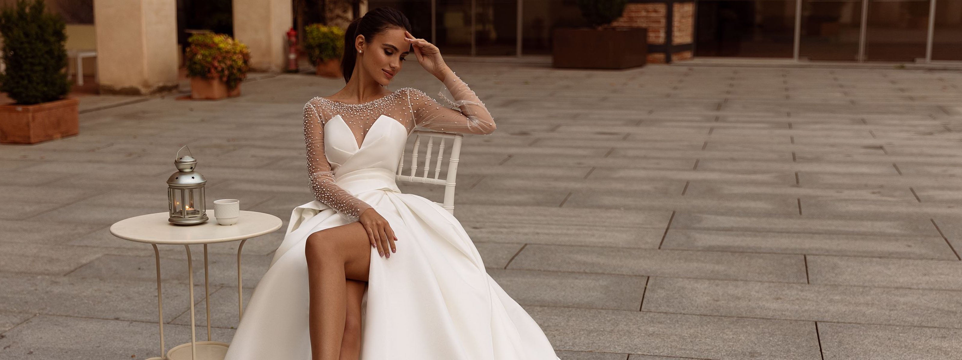 Mariée en robe Armentha à manches longues en dentelle, corsage cœur et jupe fendue avec longue traîne, assise sur une chaise en extérieur