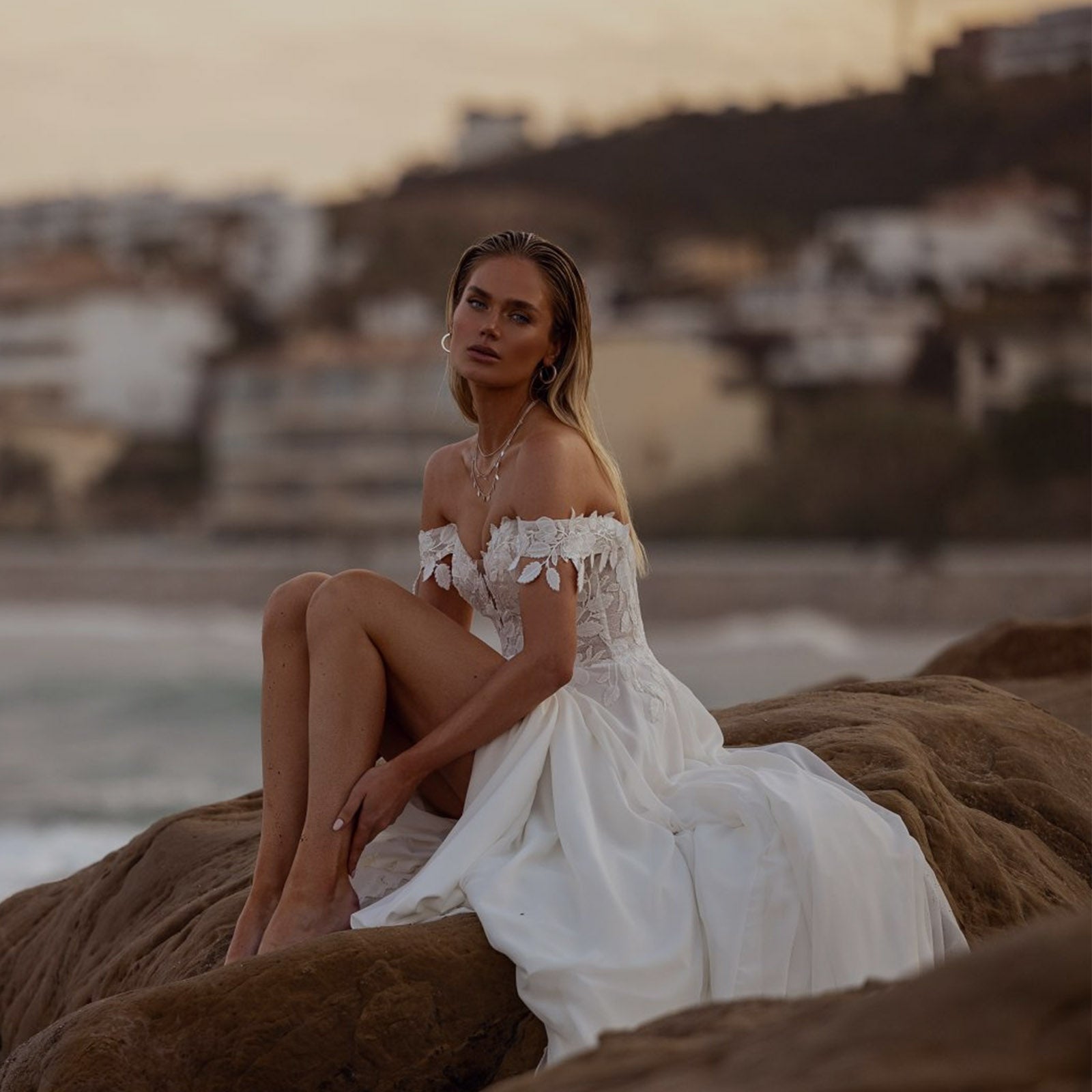Robe de mariée Anna Sposa, coupe trapèze avec épaules dénudées et dentelle florale, photographiée au bord de la mer 