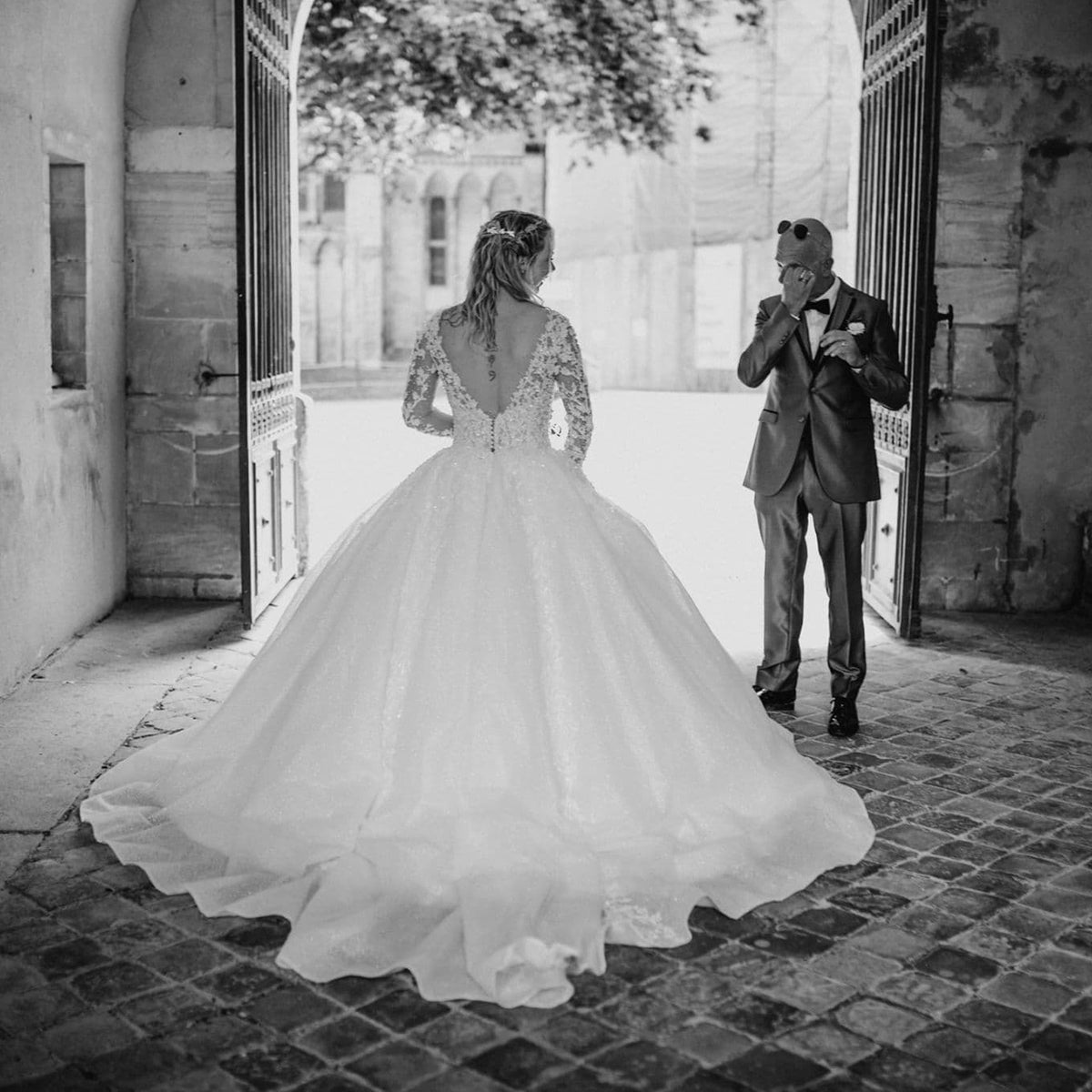 Mariée en robe princesse en dentelle avec longue traîne, photographiée devant une porte monumentale